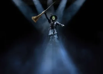 Review of Wicked el Musical in Madrid featuring Cristina Picos as Elphaba wearing a black dress, witch's hat, and cap with beams of light shining on to and from her.