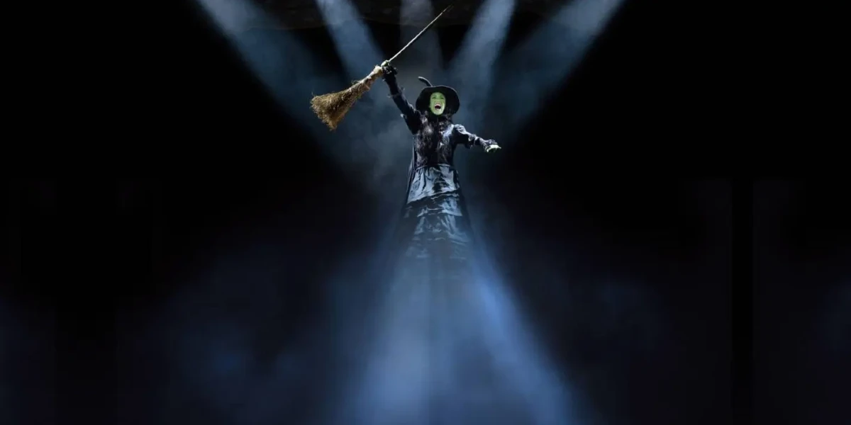 Review of Wicked el Musical in Madrid featuring Cristina Picos as Elphaba wearing a black dress, witch's hat, and cap with beams of light shining on to and from her.